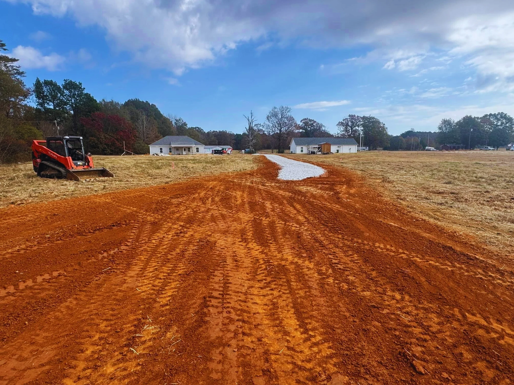 skid steer grading a red dirt driveway during a residential dirt work project in north mississippi.